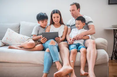 Woman, man, and two children sitting together on a couch looking at a tablet