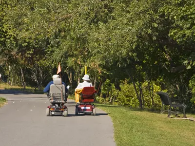 Two people on electric scooter mobility devices on a park trail