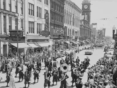 Historic photo, black and white image, band walking down a downtown street, crowds along the street