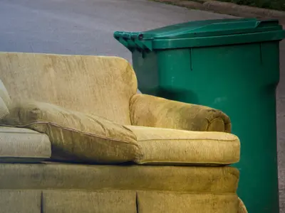 An old couch at side of road next to a Green Bin
